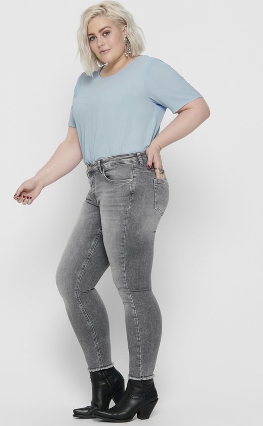 Vrouw in grijze skinny jeans met rafelende zoom en lichtblauwe t-shirt.