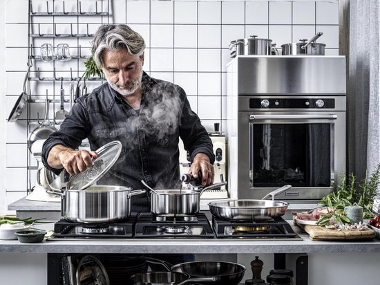 Man met grijze haren kookt in een moderne keuken met roestvrijstalen pannen.