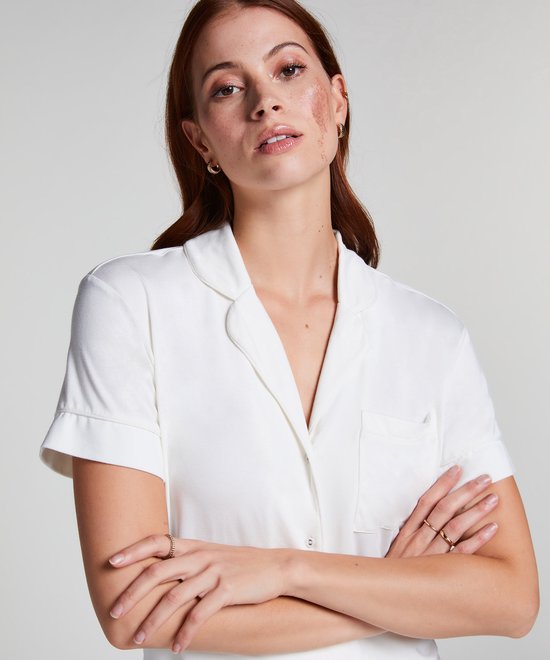 Model met rode haardos en sproeten, gekruiste armen, in een wit pyjamashirt met korte mouwen, kraag en borstzakje.