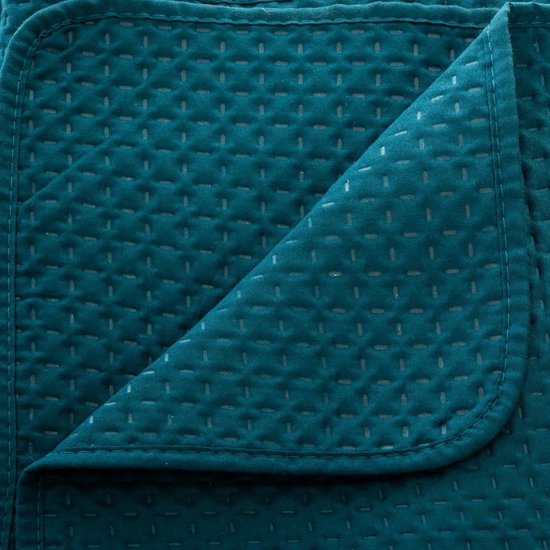 Detail van een donkergroene, geweven sprei met een subtiel ruitpatroon en gestikte stippen.