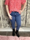 Model draagt een blauwe 3/4 skinny jeans met een rode top met grafische print.