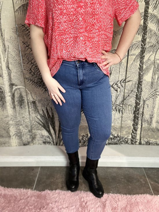 Model draagt een blauwe 3/4 skinny jeans met een rode top met grafische print.