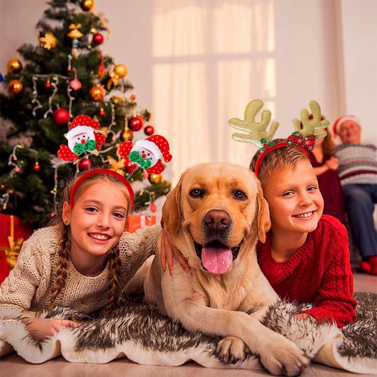 Deux enfants et un chien sont couchés sur un tapis près du sapin. La fille porte un serre-tête Père Noël.