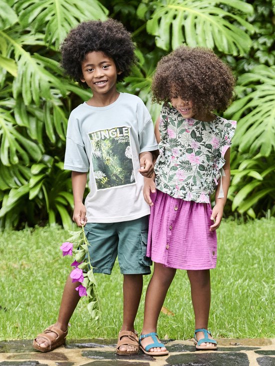 Meisje met krullend haar draagt een bloemenblouse met roze ruches en een roze rok.