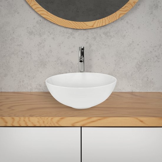 Lavabo rond en céramique blanche avec un robinet chromé sur un plateau en bois pour un meuble de salle de bain.