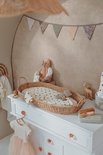 Witte commode met rotan aankleedmand, babykleding, speelgoed en een regenboogdecoratie.