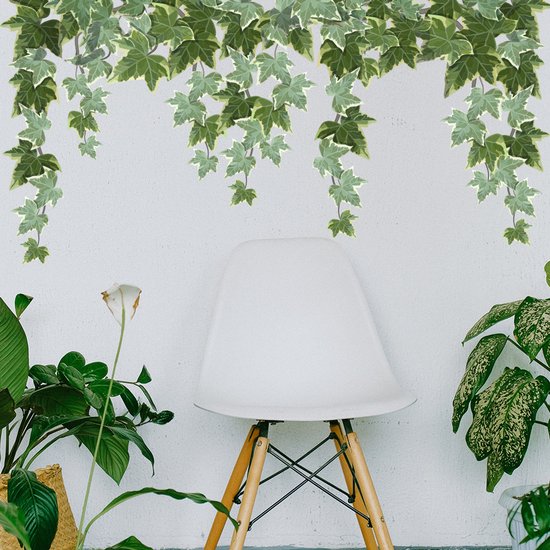 Des lianes de lierre vertes au-dessus d'une chaise blanche aux pieds en bois, flanquée de plantes.