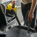 Een persoon gebruikt een gele en zwarte Powerplus nat-droog stofzuiger om een autostoel schoon te maken.