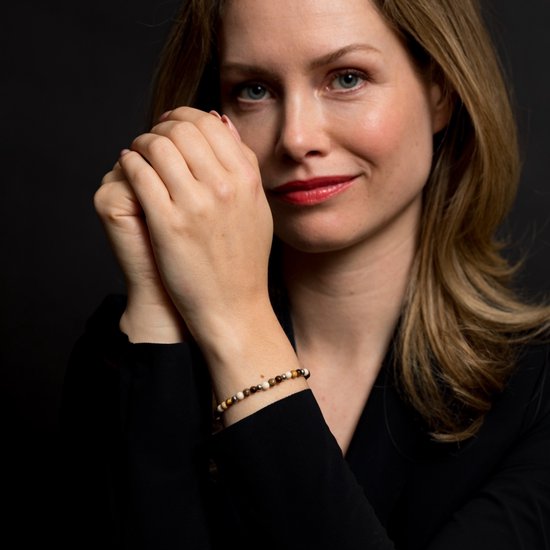 Vrouw met blonde haren draagt een armband met bruine en gouden kralen om haar pols.