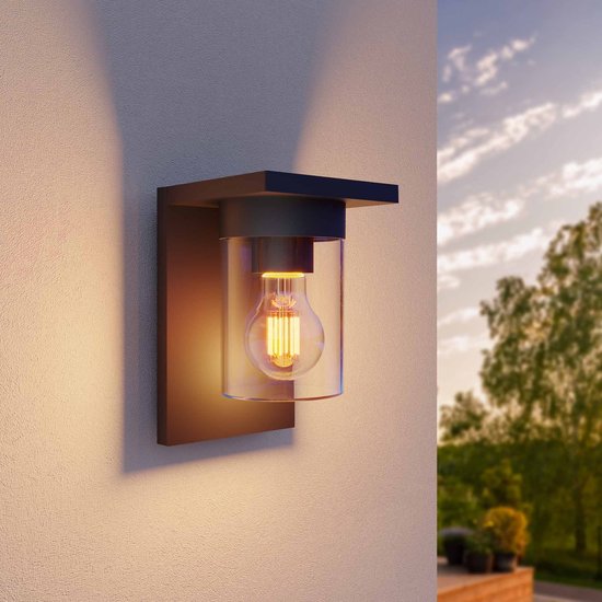 Donkere wandlamp met glazen kap en E27 gloeilamp, verlicht de muur, buiten bij zonsondergang.
