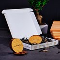 Boîte cadeau ouverte contenant des sous-verres en bois, du matériel de remplissage et de petits éléments décoratifs.