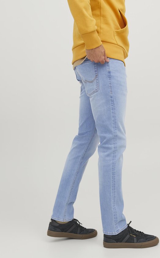 Model van opzij, draagt lichtblauwe slim fit jeans met contrasterende stiksels op de achterzak.