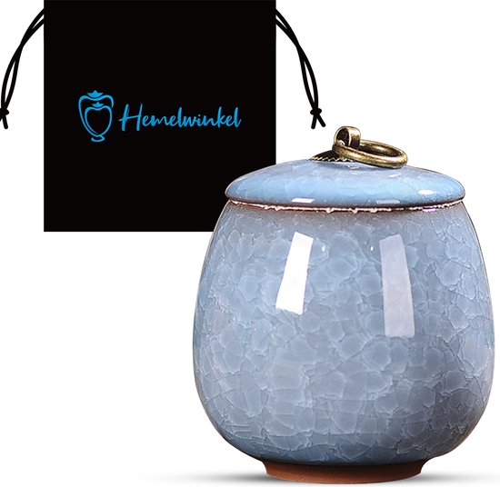 Hemelsblauwe keramische pot met deksel en gouden ring, naast een zwart stoffen zakje met logo.