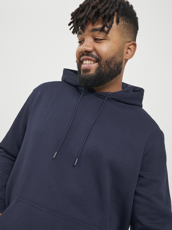 Close-up van een man met een brede glimlach in een donkerblauwe hoodie met trekkoordjes.