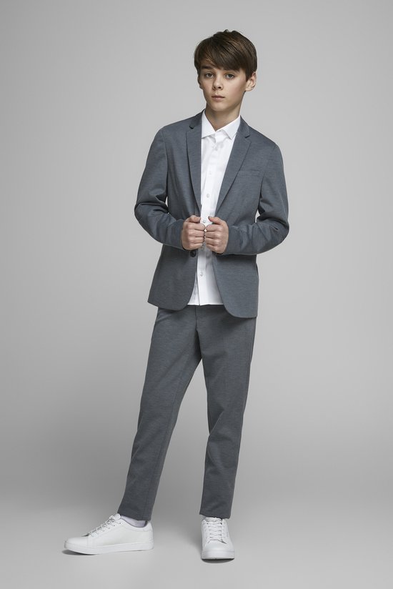Garçon en costume gris avec chemise blanche, debout.