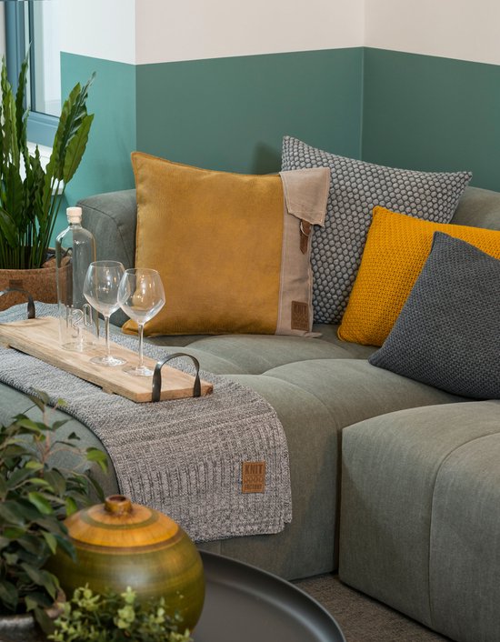 Canapé vert foncé avec des coussins moutarde et gris, un plaid gris et un plateau en bois.