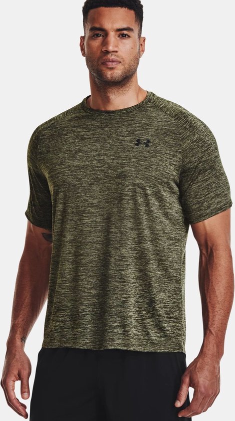 Man draagt een olijfgroen gemêleerd Under Armour sportshirt met korte mouwen en zwart broekje.