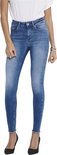 Vrouw met lang bruin haar, draagt blauwe skinny jeans met rafelige zoom en witte top, gedragen met zwarte pumps.