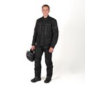 Man in een zwarte motorjas en -broek van DXR, met helm in de hand.