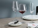 Une table dressée avec trois verres : deux verres à vin, dont un avec du vin rouge, et une flûte à champagne.
