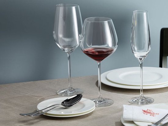 Une table dressée avec trois verres : deux verres à vin, dont un avec du vin rouge, et une flûte à champagne.