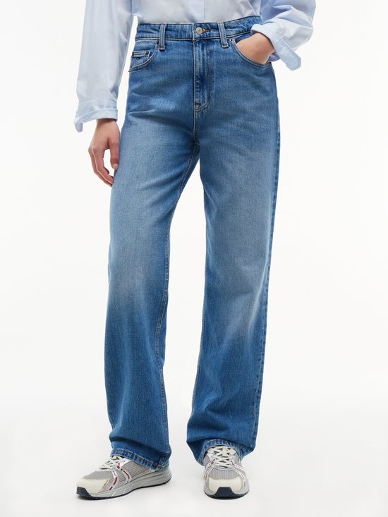 Model draagt een rechte spijkerbroek in middelblauwe wassing en een lichtblauwe blouse.