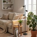Zwarte staande lamp met drie spots naast een bank in een lichte woonkamer.