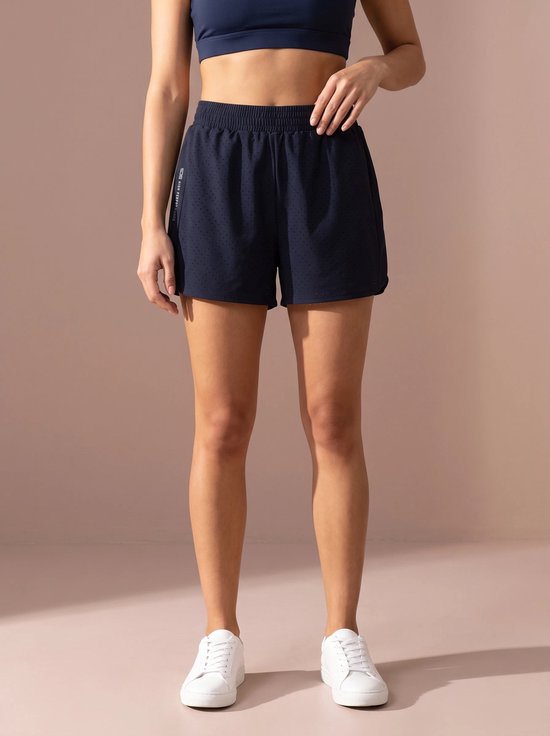 Vrouw in een donkerblauwe sportshort met perforaties en de tekst 'SJS HIGH PERFORMANCE'.