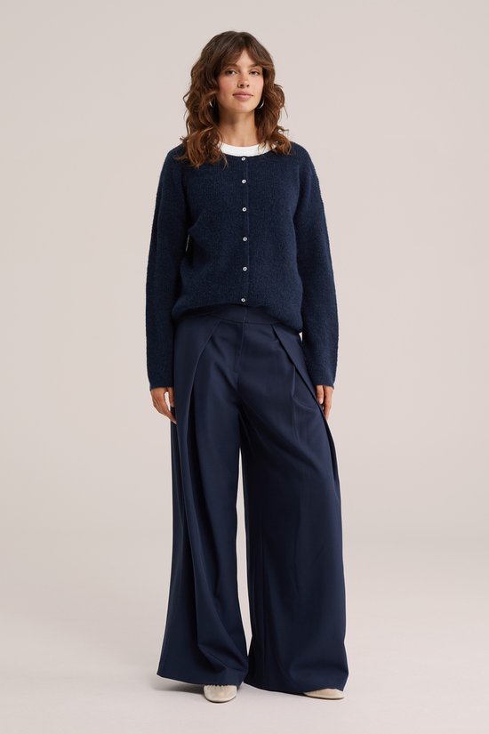Model draagt donkerblauw gebreid vest met witte top eronder