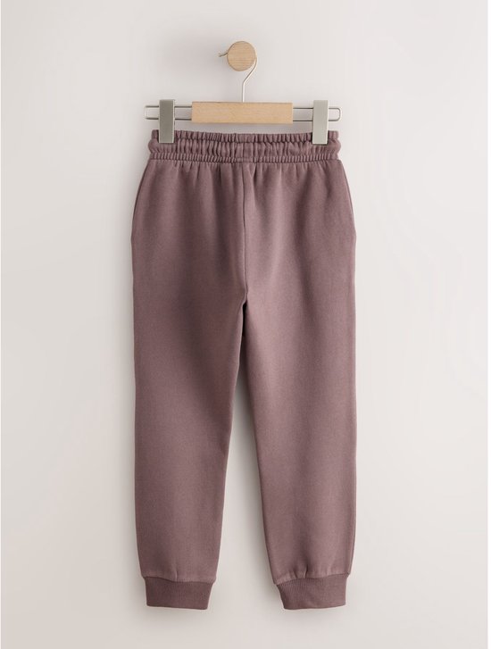 Bruine joggingbroek met trekkoord en elastische tailleband, hangend aan een kleerhanger.