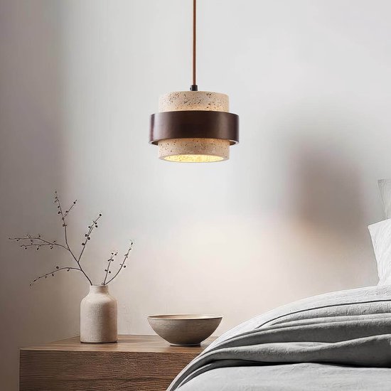 Lampe suspendue avec un cylindre en travertin et un anneau en bois foncé. La lampe est suspendue au-dessus d'une table de chevet.