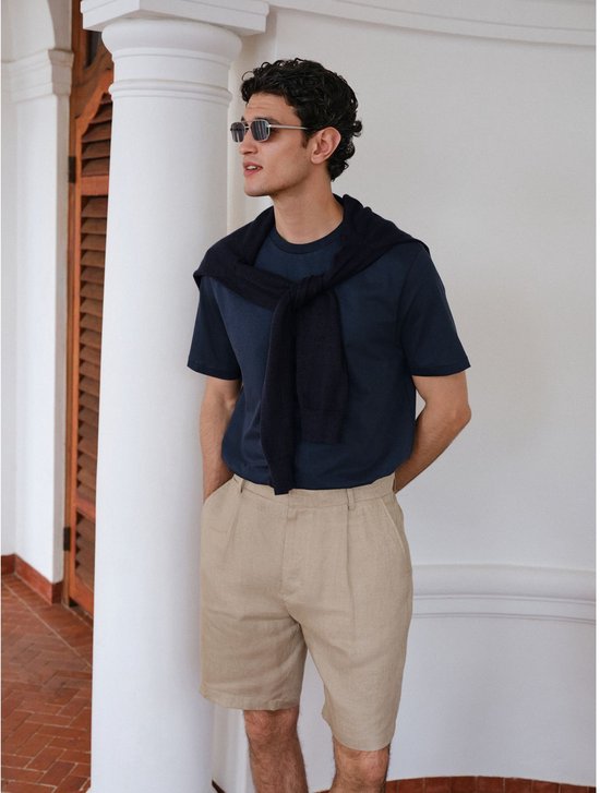 Man met donkerblauwe t-shirt, beige linnen shorts en een donkerblauwe trui over zijn schouders.