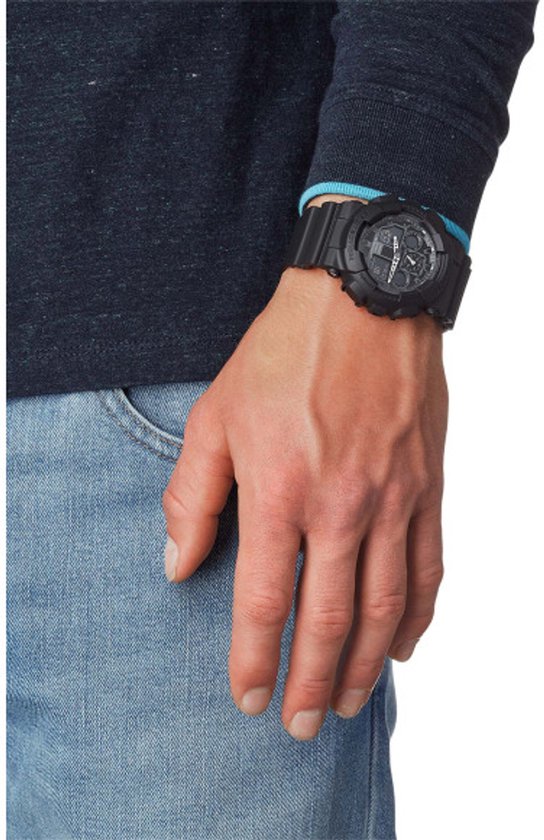 Man met spijkerbroek en donkere trui draagt een zwarte G-Shock horloge om zijn linkerpols.