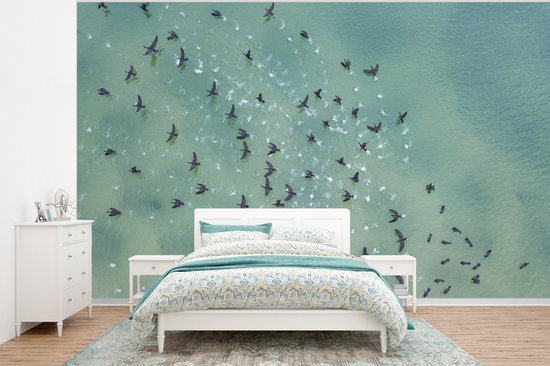 Une chambre avec un papier peint photo d'une volée d'oiseaux au-dessus d'une mer turquoise, placé derrière un lit blanc.