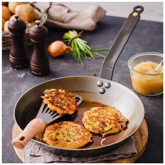 Koekenpan met drie aardappelpannenkoeken, een spatel en een potje appelmoes op een donkere tafel.