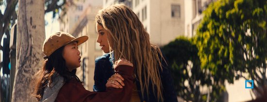 Een jonge vrouw met lange, blonde dreadlocks kijkt naar een meisje met een baseballpetje.