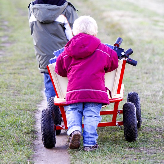 Une brouette rouge à quatre roues pleines jaunes est tirée par deux enfants.