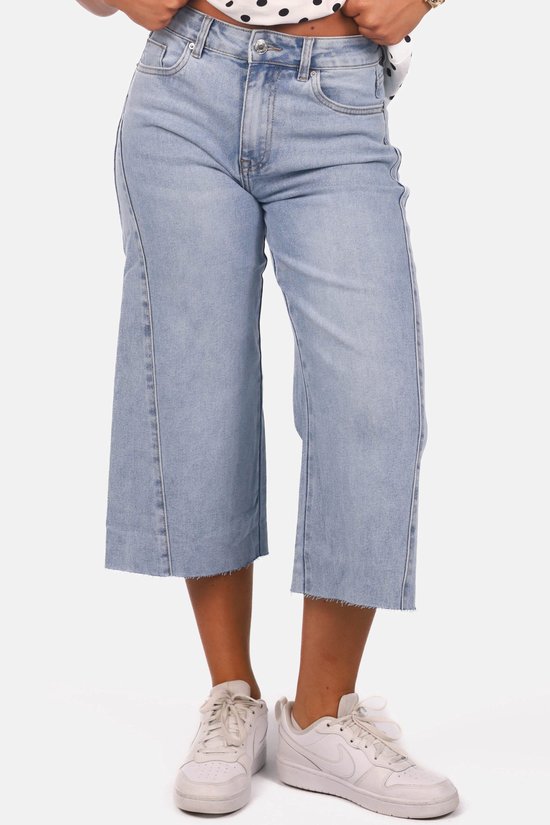 Lichtblauwe denim culotte met naaddetails en rafelige zomen, gedragen met witte sneakers.