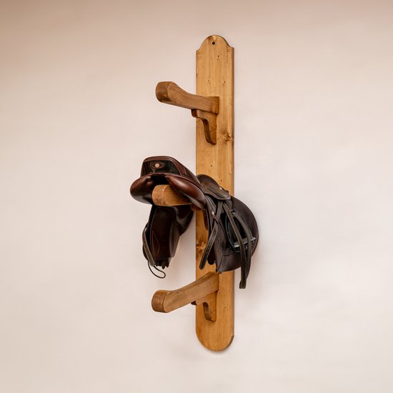 Bruin lederen zadel opgehangen aan een verticale houten wandhouder met twee steunbalken.
