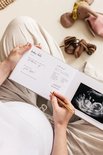 Zwangere vrouw schrijft met goudkleurige pen in 'baby date' dagboek met een ingeplakte echofoto.