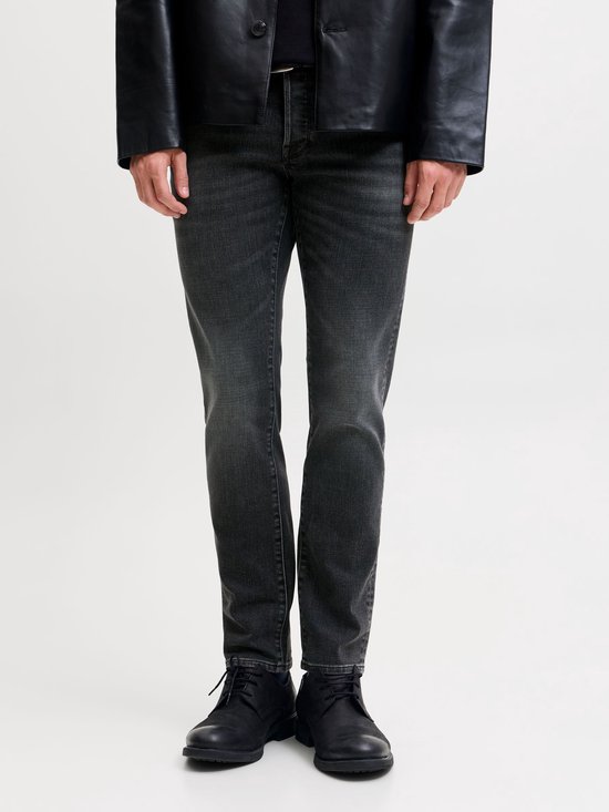 Model draagt een grijze slim fit jeans met een zwarte leren jas en zwarte schoenen.