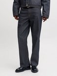 Model draagt een straight fit jeans in donkerblauw denim met contrasterende oranje stiksels.
