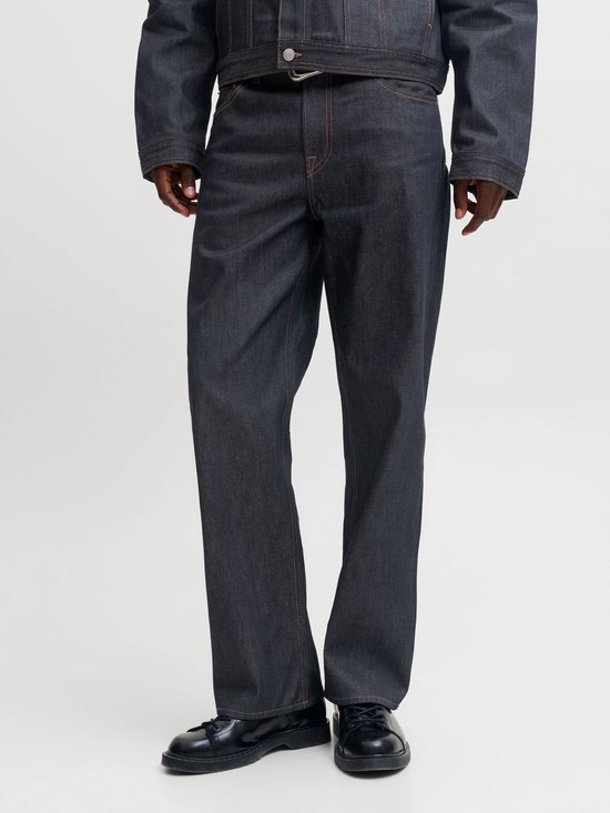 Model draagt een straight fit jeans in donkerblauw denim met contrasterende oranje stiksels.