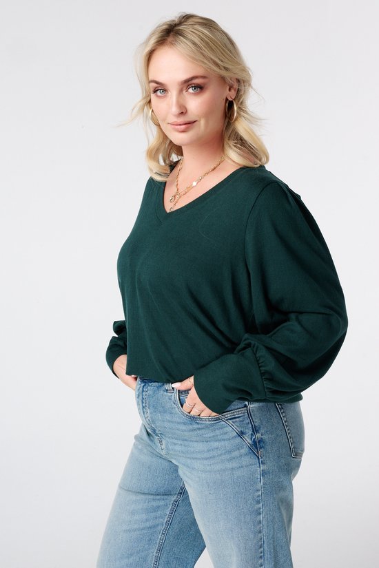 Model in donkergroene top met pofmouwen en jeans.