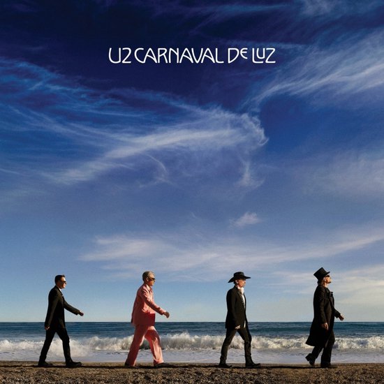 Vier mannen van U2 lopen op een strand onder een blauwe lucht. Tekst: U2 CARNAVAL DE LUZ.