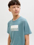 Jongen draagt blauw t-shirt met witte rechthoekige print en Jack & Jones logo op de borst.