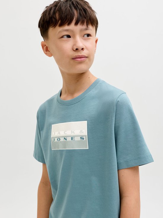 Jongen draagt blauw t-shirt met witte rechthoekige print en Jack & Jones logo op de borst.