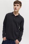Model draagt een zwarte longsleeve poloshirt met knoopjes en donkere jeans.