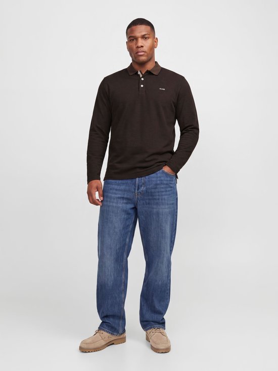 Model draagt bruine polo met lange mouwen, jeans en beige schoenen, hand in broekzak.