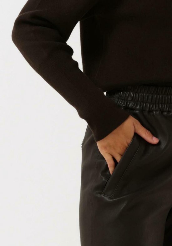 Close-up van een vrouw met handen in de zakken van een donkerbruine leren broek.